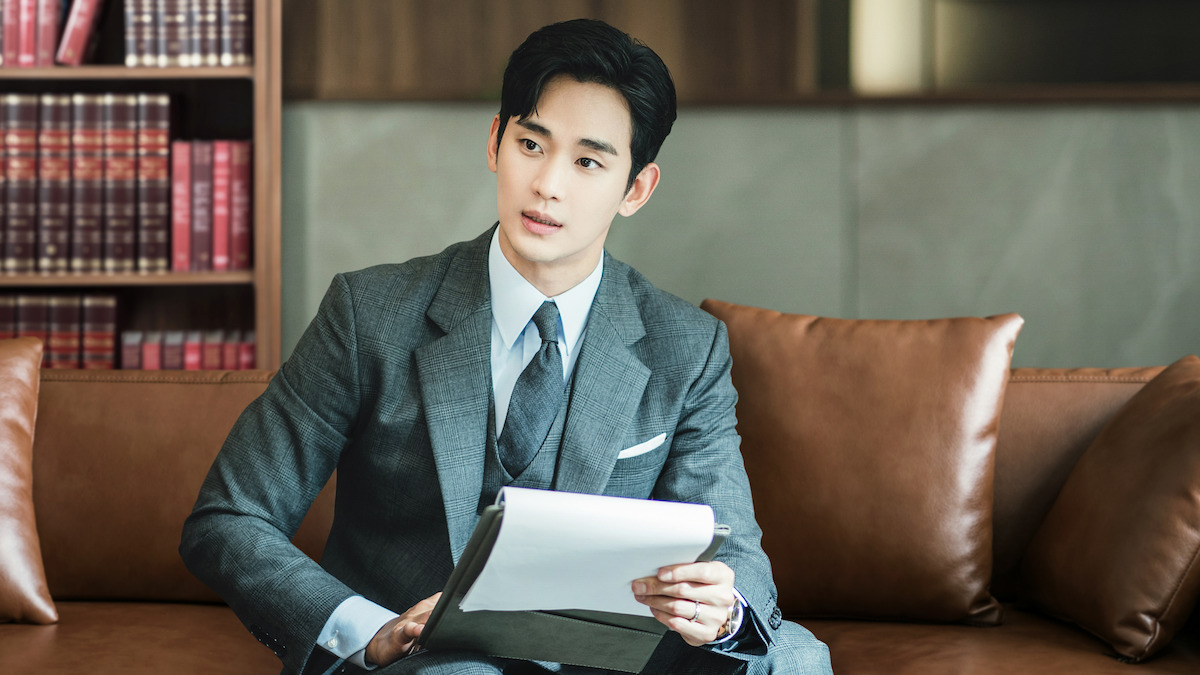 Kim Soo-hyun as Baek Hyun-woo sits on a leather sofa wearing a gray suit in the series ‘Queen of Tears.’