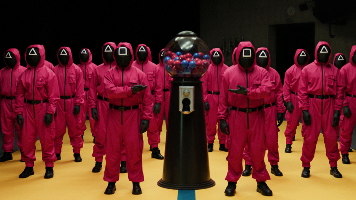 'Squid Game' Masked Guards in a room surrounding a large gum ball machine.