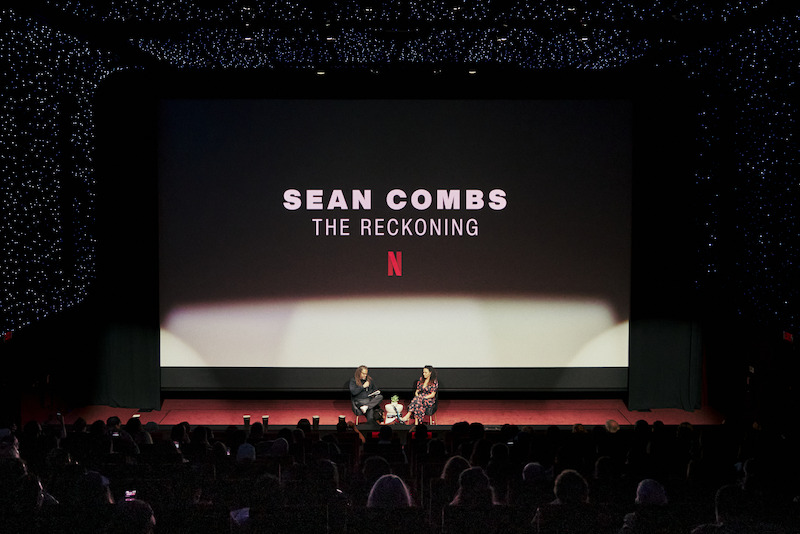 A theater with a stage with two people in chairs sitting on it.