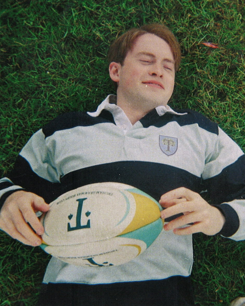 Disposable photo of Kit Connor as Nick Nelson laying in the grass in a striped polo shirt in Heartstopper Forever