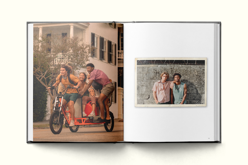 Four friends ride a tandem bike outside a house on the left page, while two friends stand together, smiling by a textured wall in a smaller photo on the right page of an open photo book.