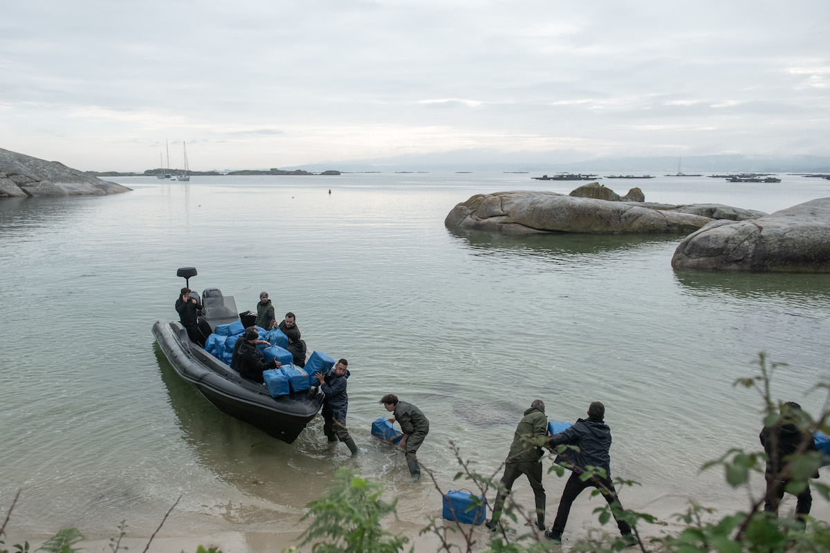 A group of men carry blue containers on to a small boat in ‘Gangs of Galicia’