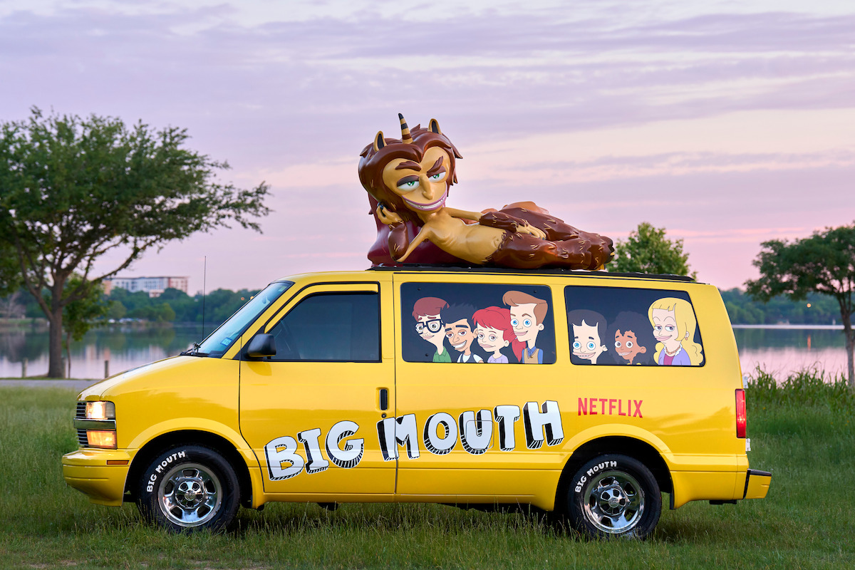 A yellow van with the cast of ‘Big Mouth’ in the windows, with the Hormone Monster lying on top of it.