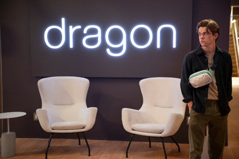  John Owen Lowe as Jackson stands in front of a wall with a neon sign with the "Dragon" logo in Season 2 of 'Unstable'