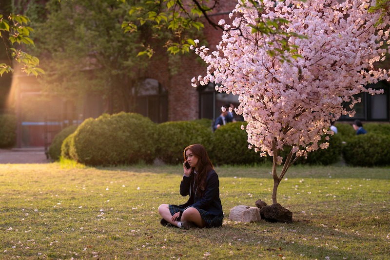 Anna Cathcart as Kitty Song Covey sits under a tree with pink blossoms in Season 2 of 'XO, Kitty'