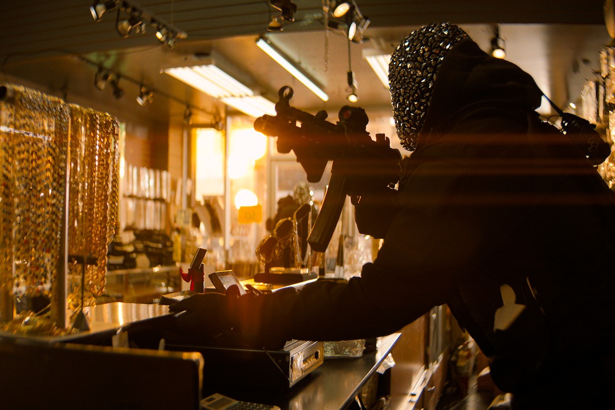A masked person holding a rifle robs a jewelry store at sunset, surrounded by glass display cases with gold chains, dramatic light streaming in through the windows.