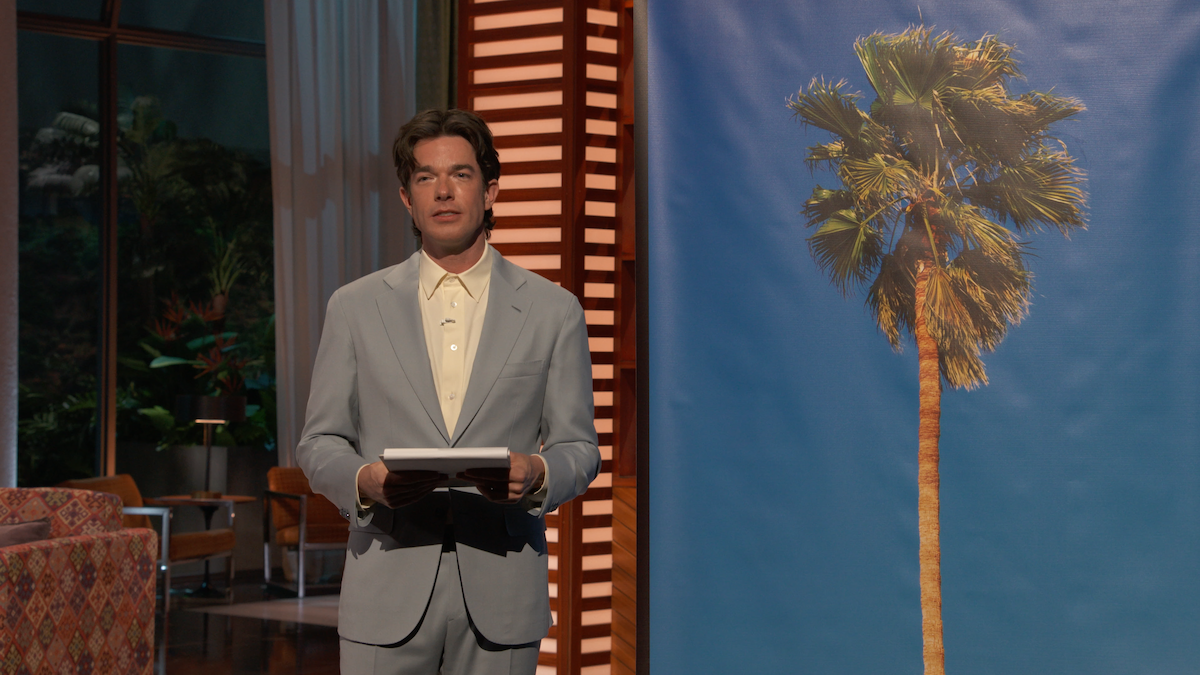 John Mulaney stands next to a picture of a palm tree