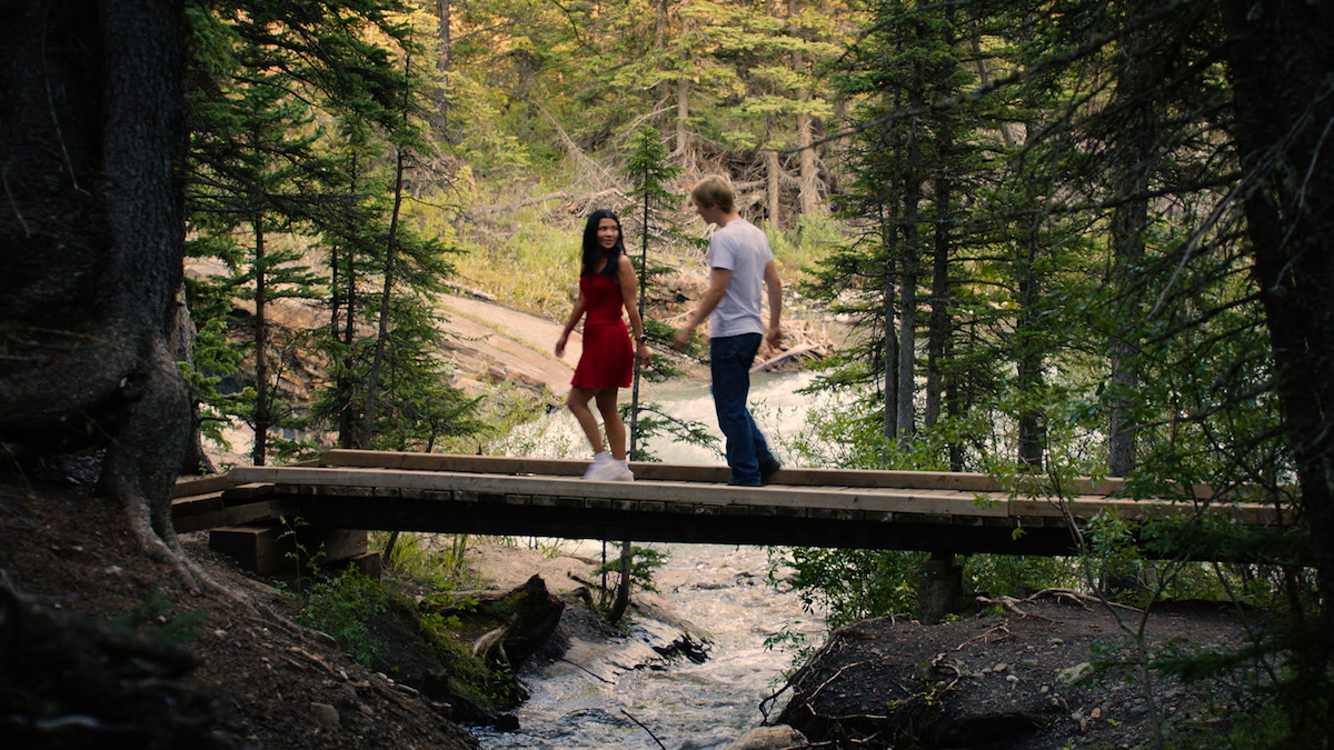 Jackie and Cole walk across a bridge in a forest