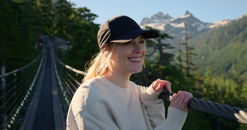 Alexandra Breckenridge as Mel Monroe smiles on a rope bridge with a mountain in the background in Season 5 of ‘Virgin River.’
