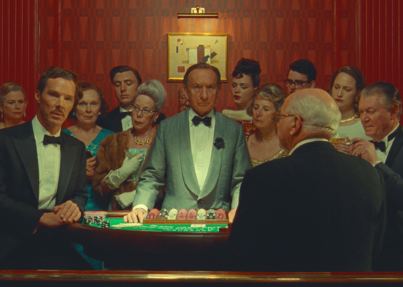 Benedict Cumberbatch as Henry Sugar and Ben Kingsley as Croupier stand in a group of people gambling in 'The Wonderful Story of Henry Sugar.'