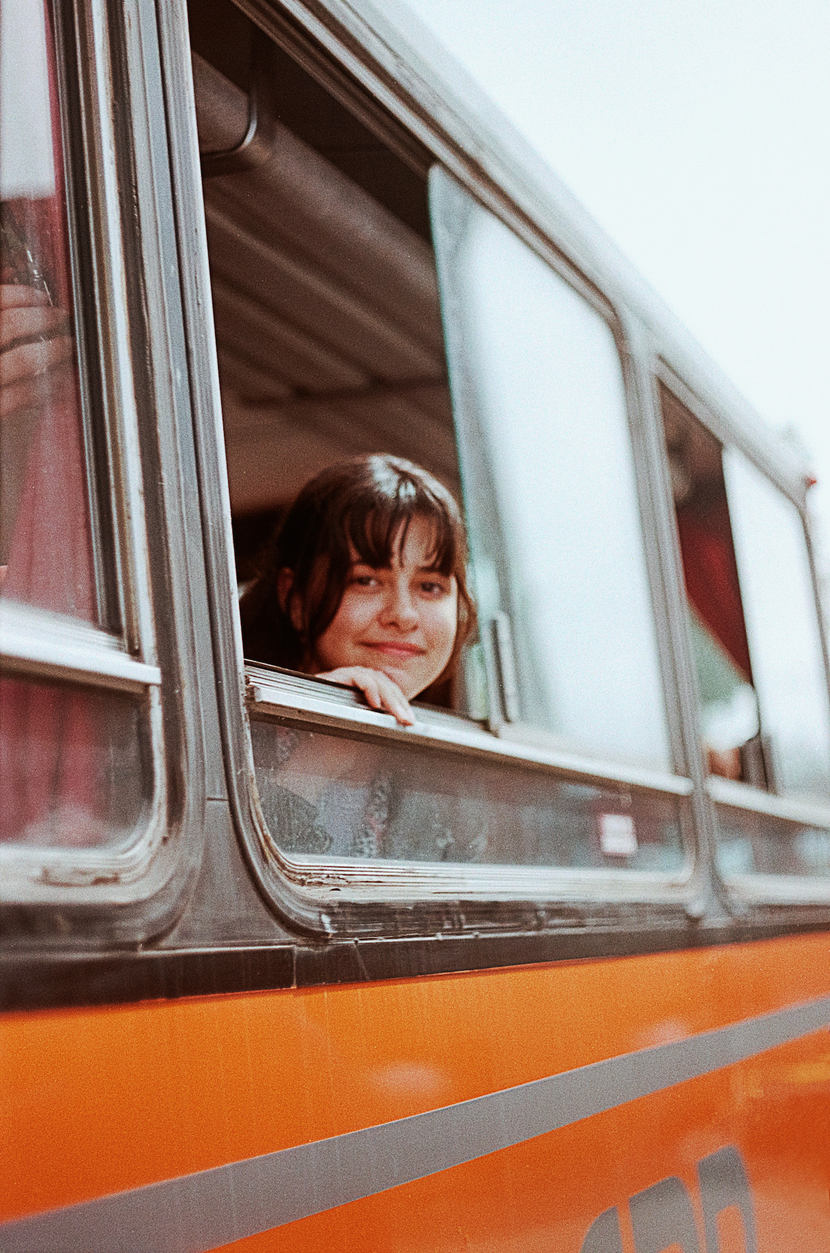 Grace Edwards peeks out of a bus window on set of Jay Kelly in Italy.