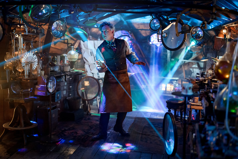 Inventor in a cluttered workshop surrounded by gadgets, glowing lights, and mechanical devices, with blue laser beams cutting through the air, creating a magical and mysterious atmosphere.