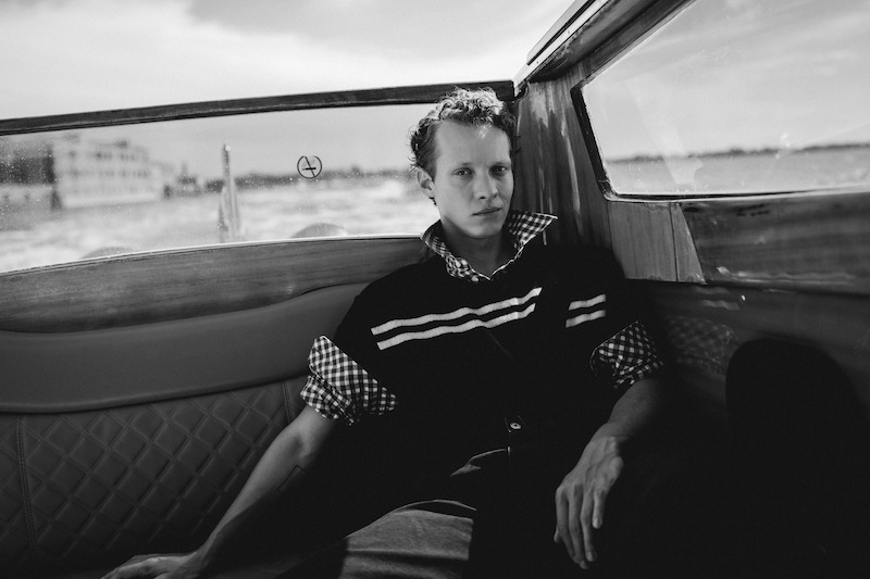 Felix Kammerer lounges in a boat in the Venice canals in a striped sweater.