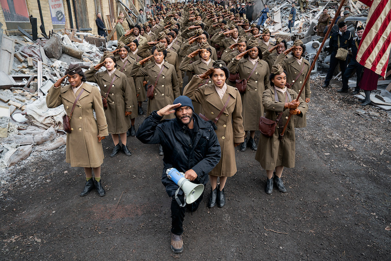 Behind the scenes photo of Tyler Perry in the middle of a large cast dressed in military clothing. 