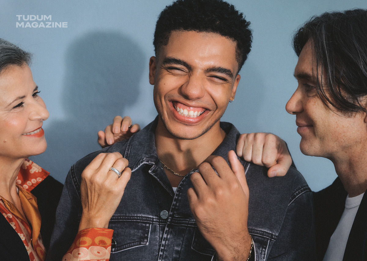 From left to right, Tracey Ullman, Jay Lycurgo, and Cillian Murphy caught in a moment of joy on set in front of a light blue wall.