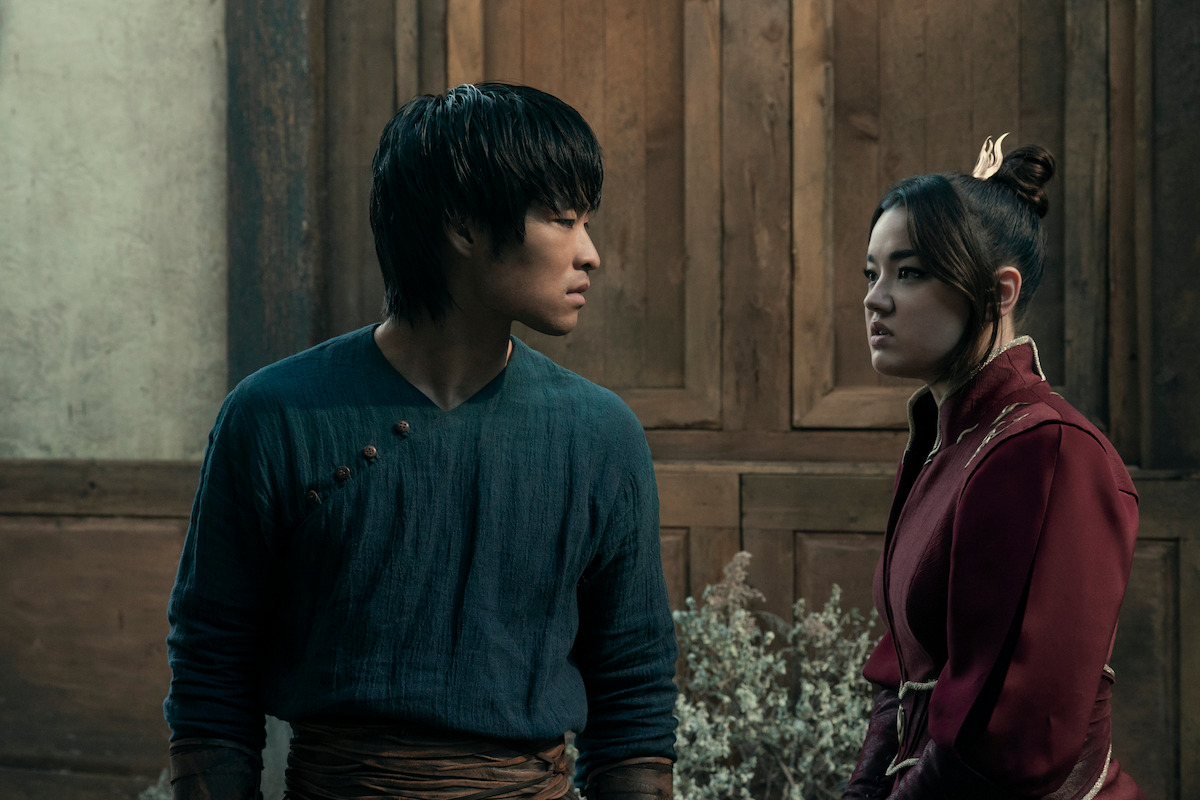 Zuko and Azula in traditional clothing stand indoors facing each other, appearing serious. The background shows a wooden wall and dried plants, suggesting a historical or fantasy setting.