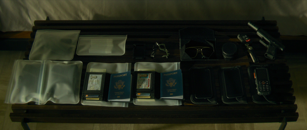 An array of passports, phones, and sunglasses lie in a case on top of a bed in a still from ‘The Killer.’