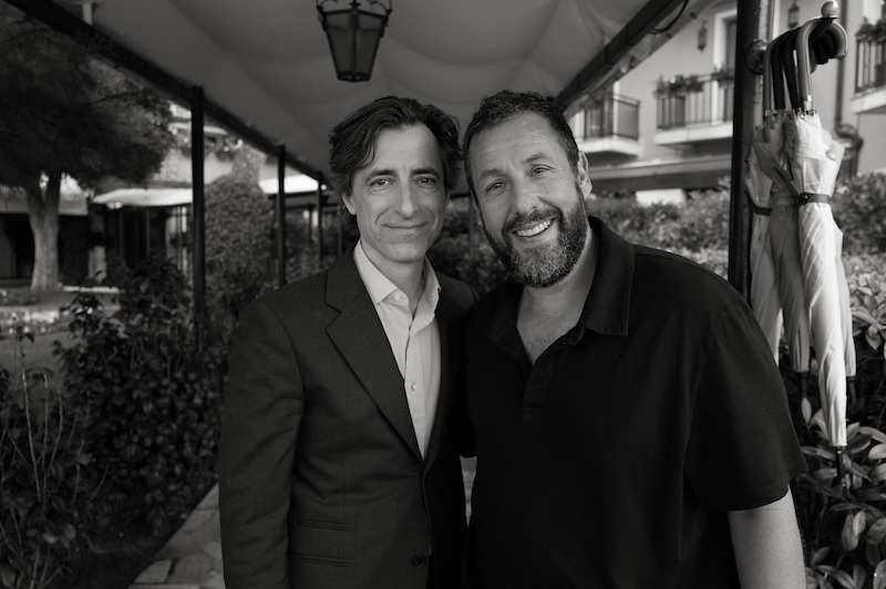 Noah Baumbach, in a blazer, and Adam Sandler, in a polo, smile and pose next to one another.