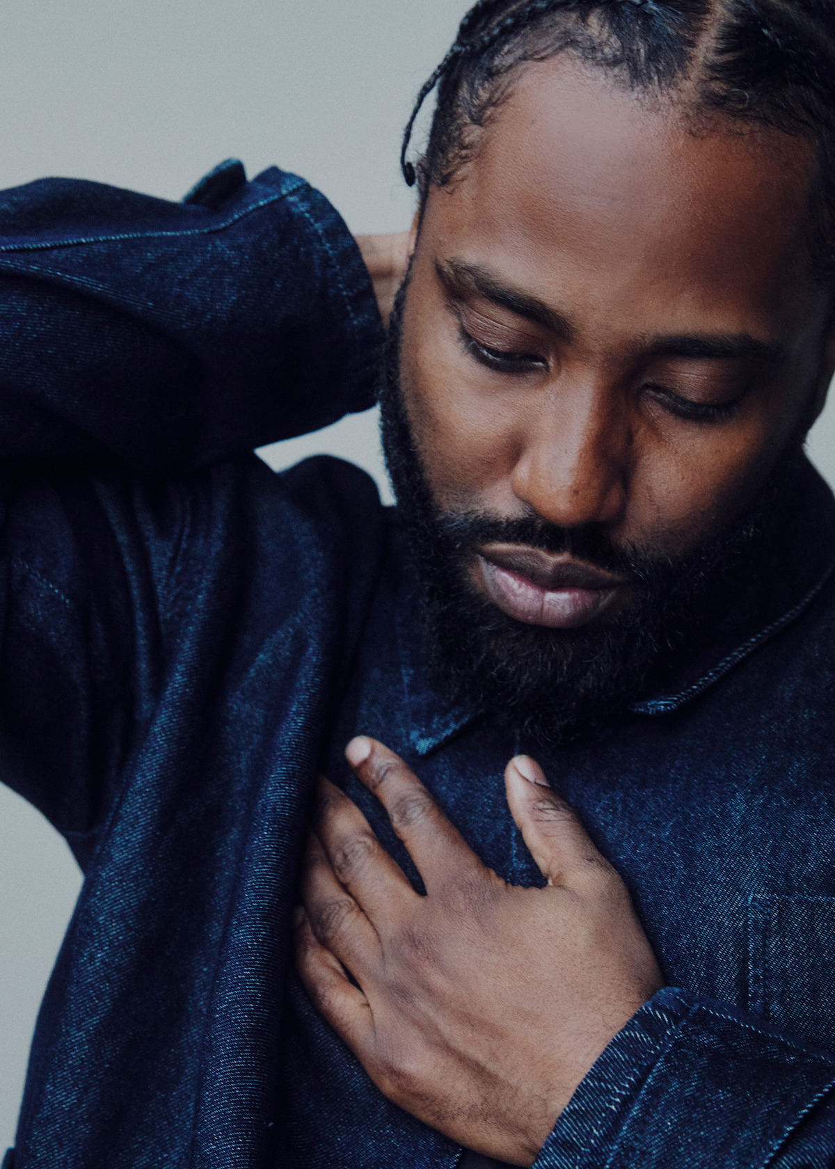 John David Washington wears a dark blue long-sleeved and holds his hand to his heart.