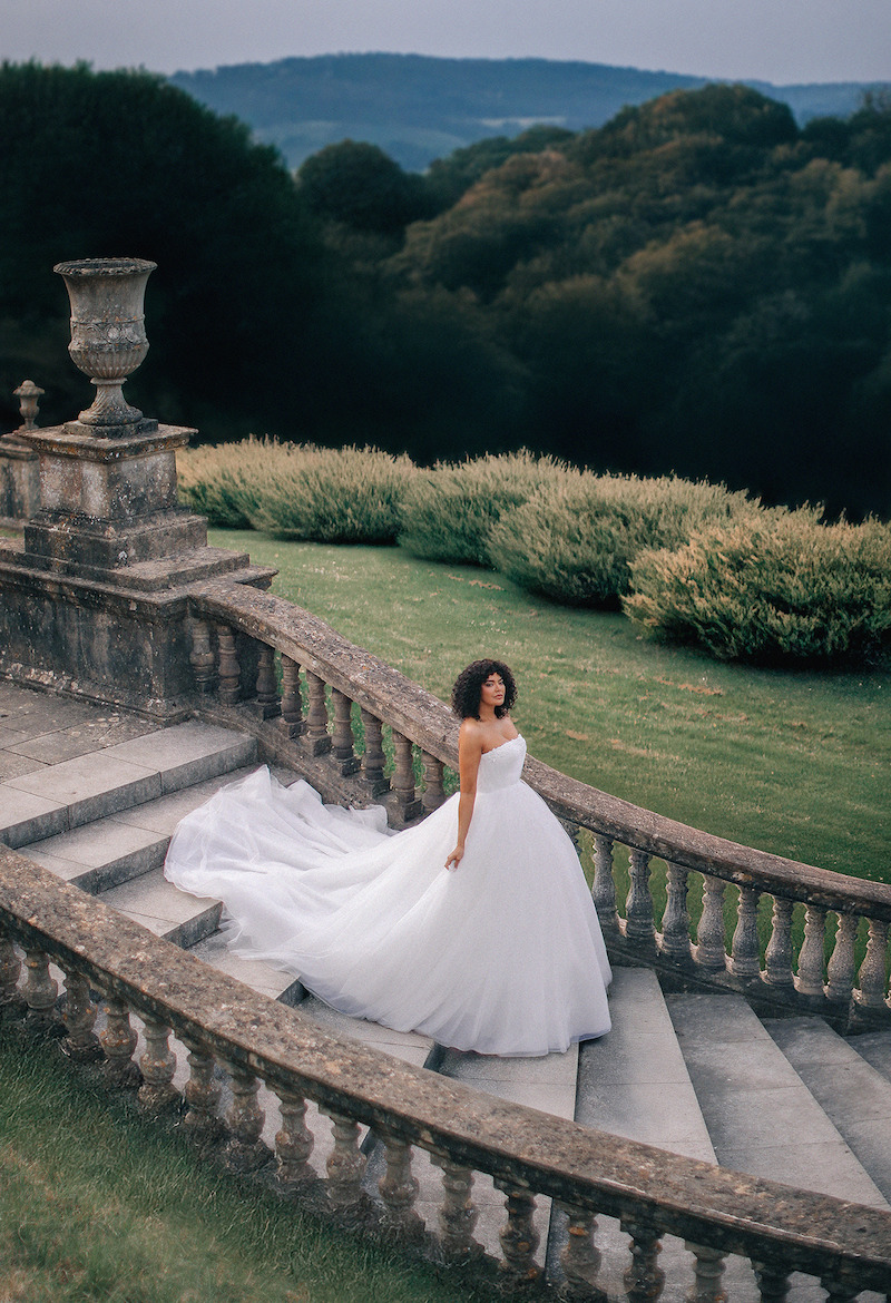Woman in bridal dress walks down stairs.