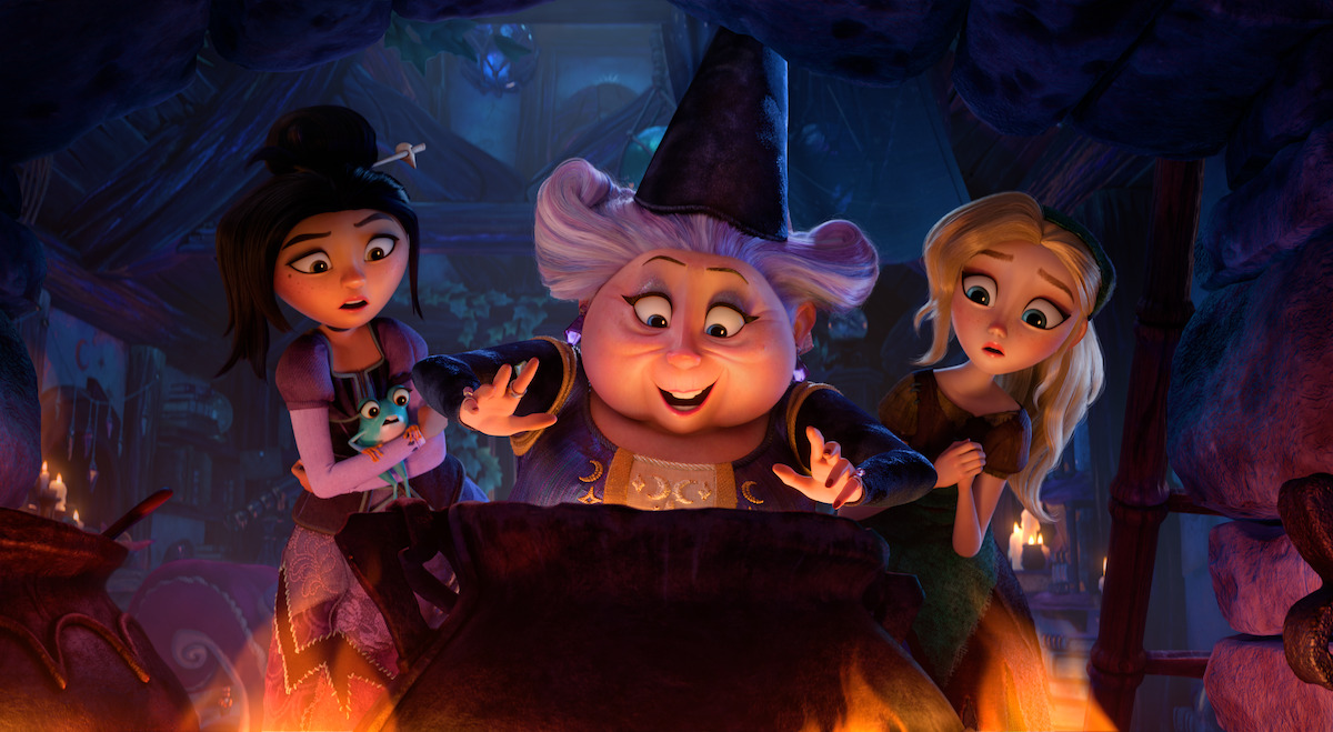 Three animated characters, including a cheerful witch in a hat, stand around a bubbling cauldron in a mystical, fire-lit room, with magical and curious expressions.
