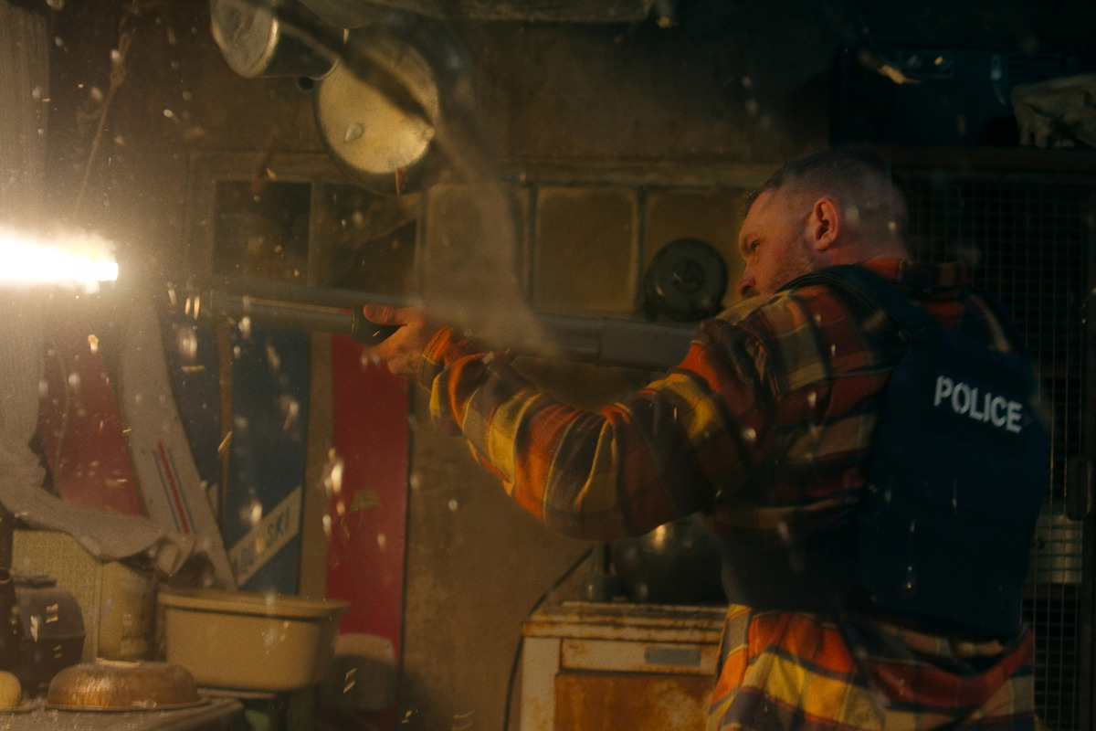 Tom Hardy as Walker shoots a large gun in a shack in 'HAVOC'