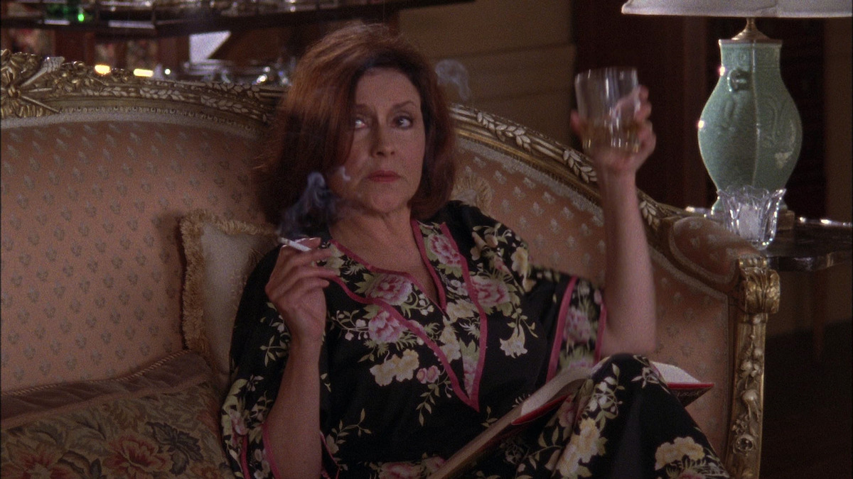 A woman sits on a sofa with a drink and a cigarette