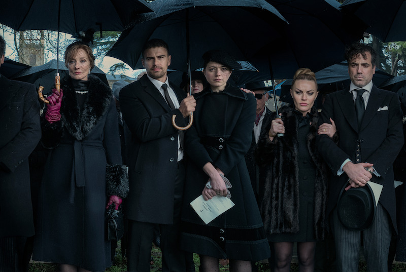 Joely Richardson, James, Jasmine Blackborow, Chanel Cresswell, and Ings stand holding umbrellas and wearing all black in Season 1 of ‘The Gentlemen.’