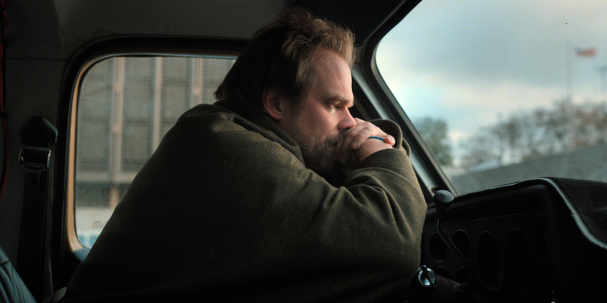 Man sitting alone in a vehicle, leaning on the steering wheel with a thoughtful expression.
