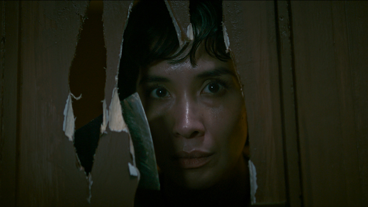 Marsha Timothy sebagai Morni melihat melalui lubang di pintu yang rusak di film tahun 2024 