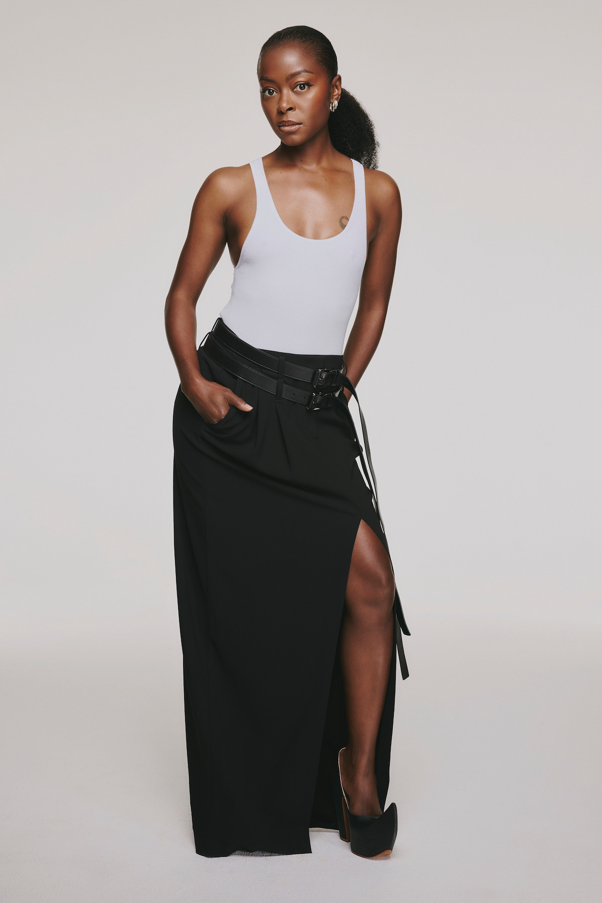 Danielle Deadwyler in a wears a black skirt and white tank against a white background.