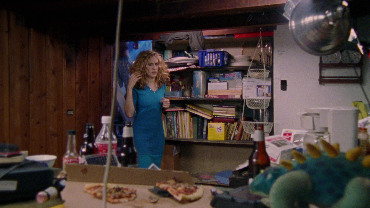 Carrie in a blue dress looks at leftover pizza in a box. 