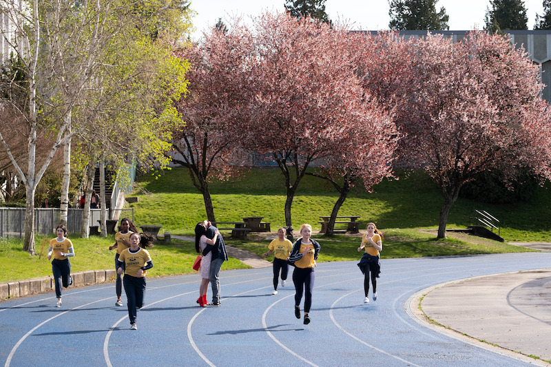 Noah Centineo as Peter and Lana Condor as Lara Jean kissing on the track as runners go by.