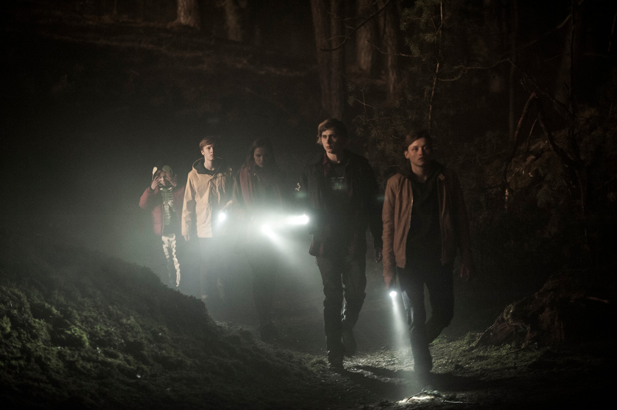 The cast of ‘Dark’ walk in the woods with flashlight. 