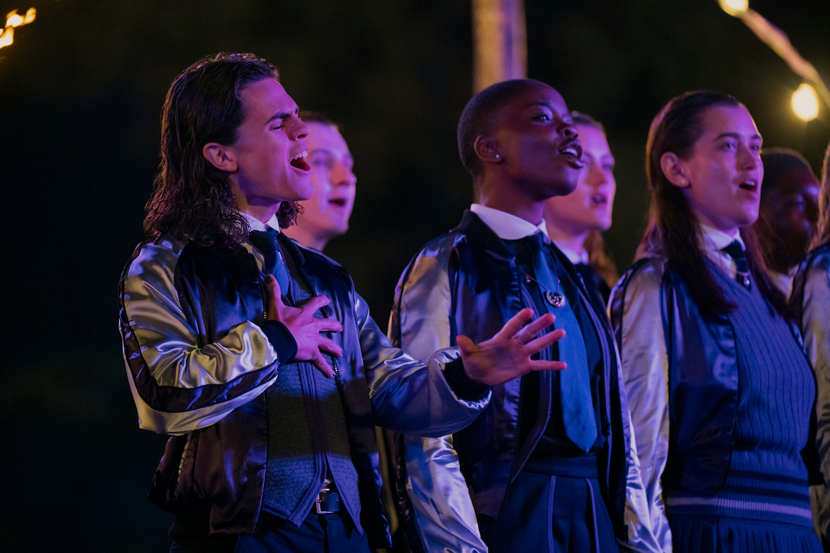 Oliver Watson as Kent and Joy Sunday as Bianca Barclay sing in a group in ‘Wednesday’ Season 2.