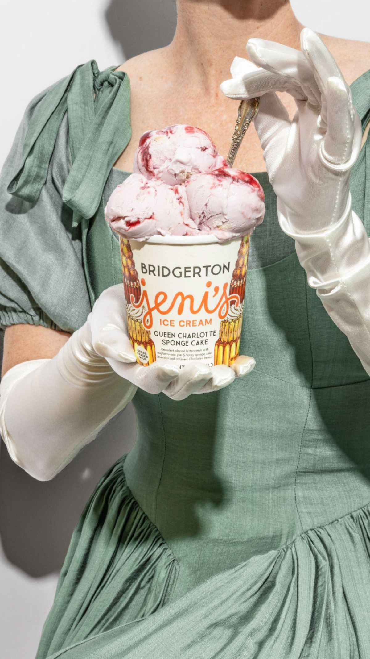 Woman in a vintage green dress and white gloves holds a pint of Jeni’s Bridgerton ice cream with a spoon, against a plain white background.