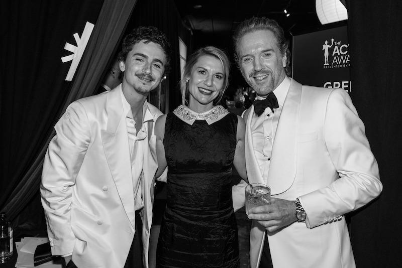 Three people, two men in white jackets and a woman in a black dress, smile for the camera.