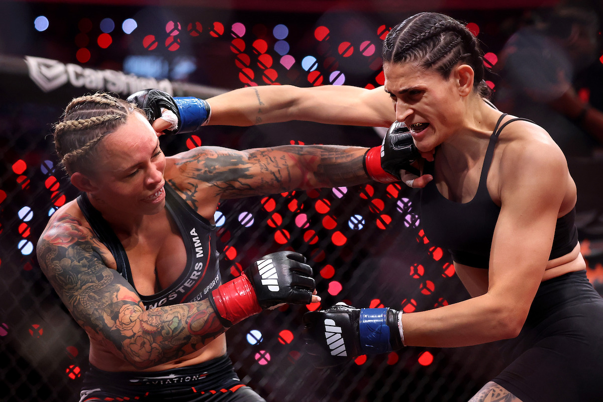 Two female MMA fighters exchanging punches inside a caged arena, wearing gloves and athletic gear, with intense expressions and dramatic lighting in the background.