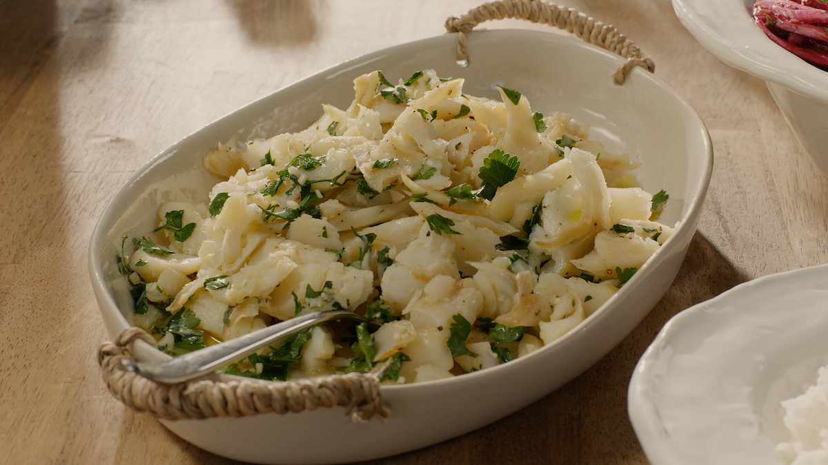 A serving dish filled with a light fish salad garnished with herbs, placed on a wooden table in a casual dining setting, evoking a fresh and inviting mood.