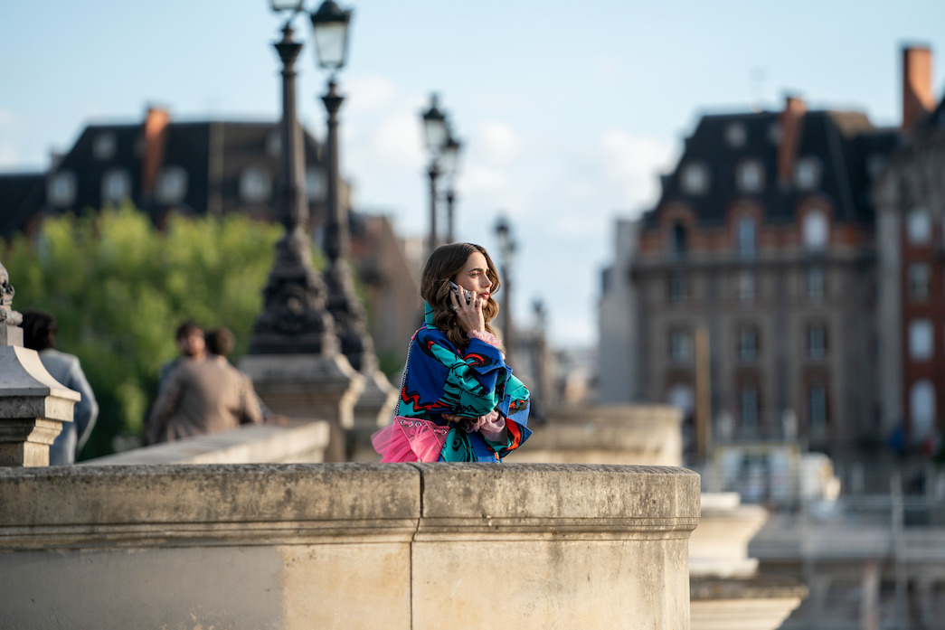 A pensive Emily stops on the Pont Neuf to make a phone call