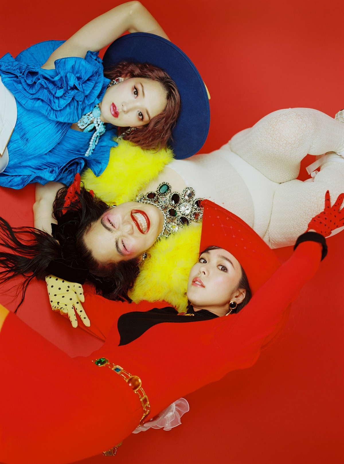 Yuriyan Retriever, Erika Karata, and Ayame Goriki pose wearing bright outfits and lay on the ground together