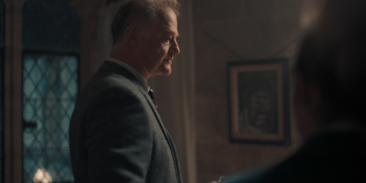 Owen Teale as Peter Knox stands in profile in a dimly lit room in an image from the series ‘A Discovery of Witches.’