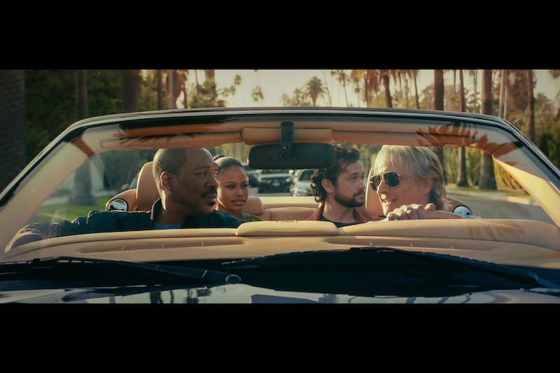 Eddie Murphy as Axel Foley, Taylour Paige as Jane Saunders, Joseph Gordon-Levitt as Detective Bobby Abbott, and Bronson Pinchot as Serge riding in a convertible car together.