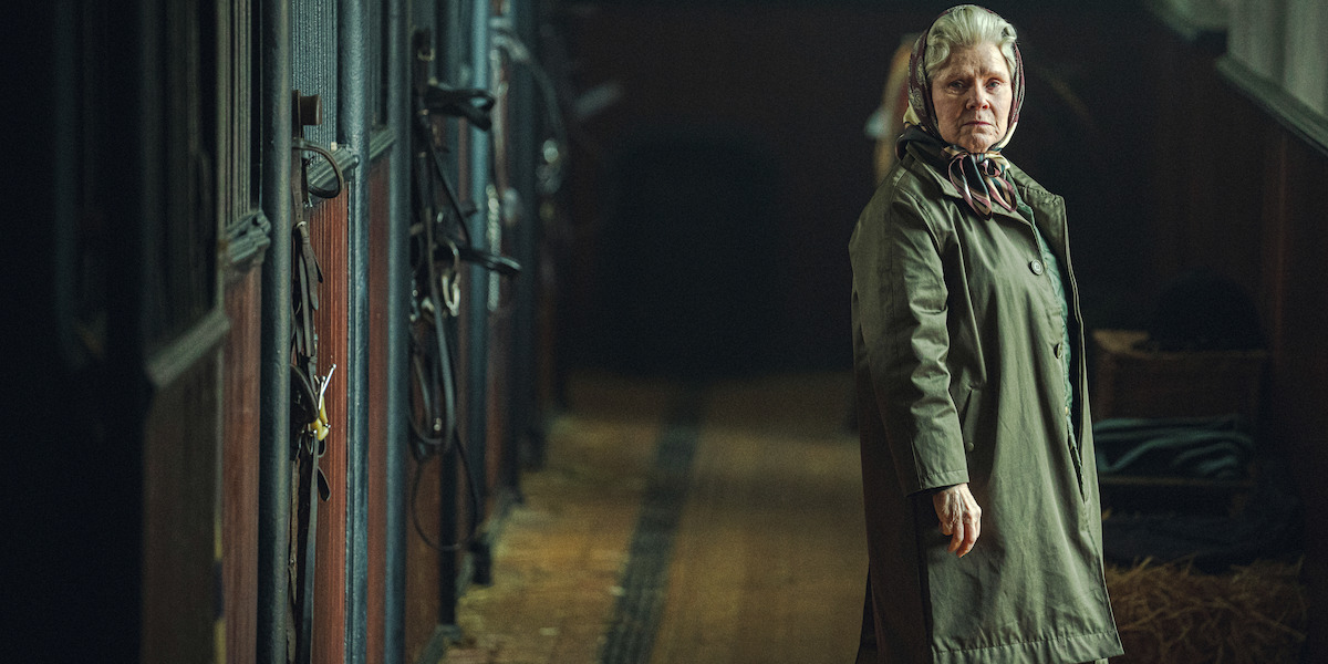 The queen standing in a horse stable.