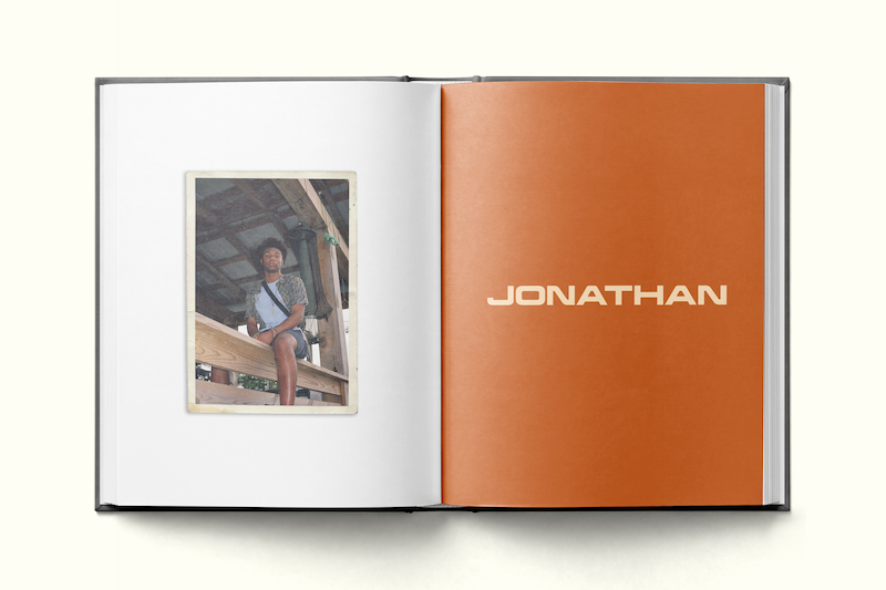 Photo book open to two pages: left page shows a person sitting in a rustic wooden structure, wearing casual clothes; right page is solid orange with the name JONATHAN in bold, modern lettering.