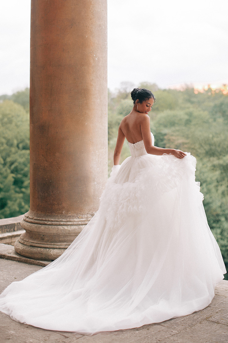 Woman in bridal dress poses next to a column.