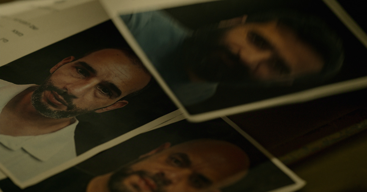 Several printed headshot photographs of men with serious expressions, arranged overlapping on a dark surface, resembling identification or investigative files in a dimly lit environment.
