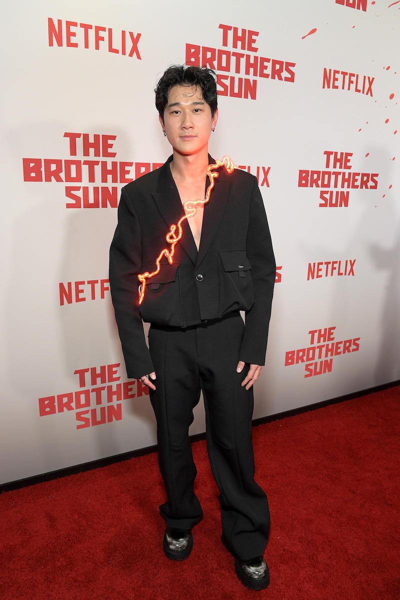 Sam Song Li attends Netflix's 'The Brothers Sun' Los Angeles Premiere at Netflix Tudum Theater wearing a black suit and a neon adornment 