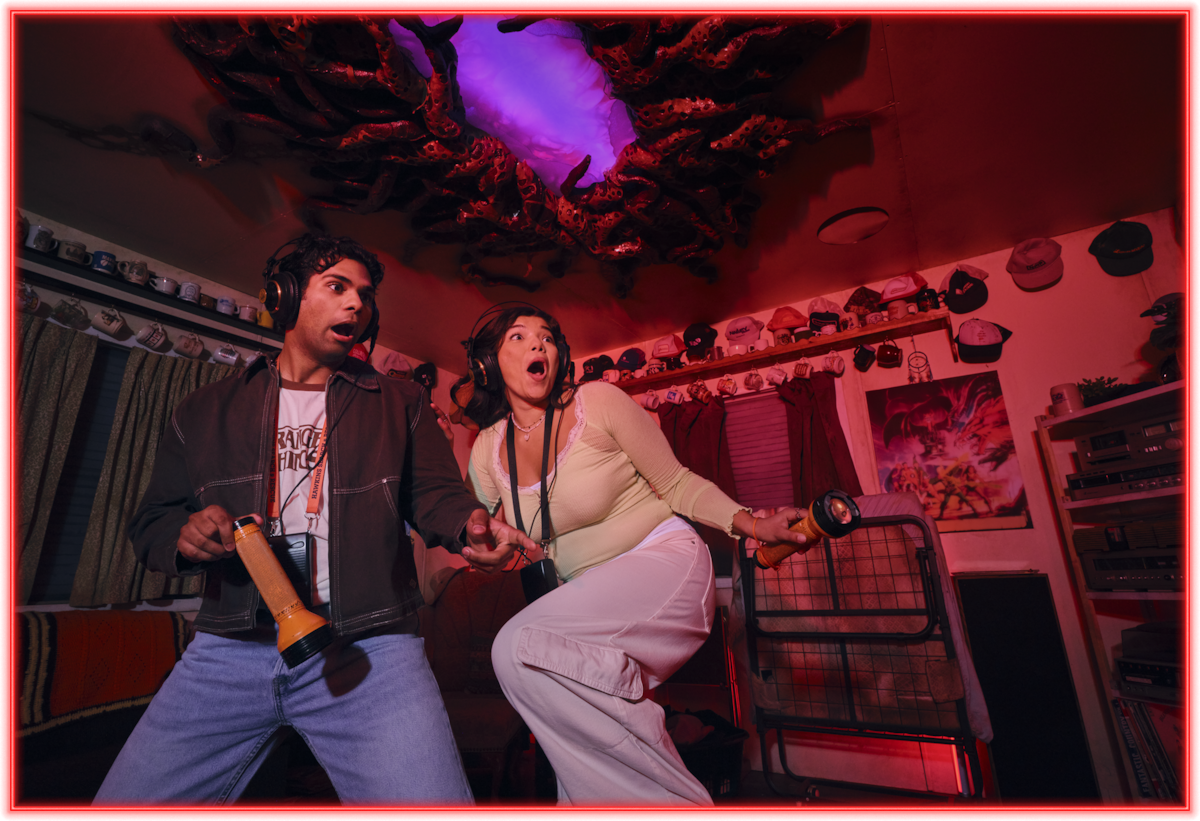 Two people wearing headphones look surprised, holding controllers in a retro living room with neon lighting, vintage decor, and a glowing, ominous portal with roots on the ceiling.