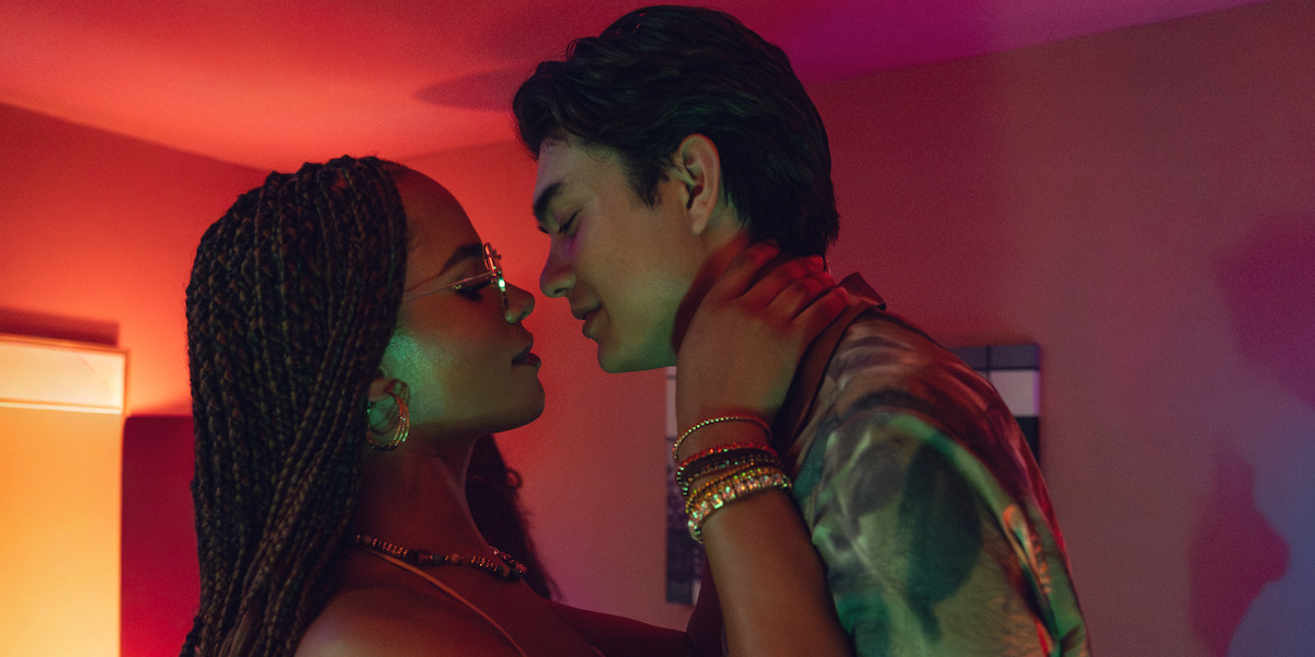 Two people in an intimate pose in a dimly lit room with colorful lighting, facing each other closely, creating a romantic atmosphere.